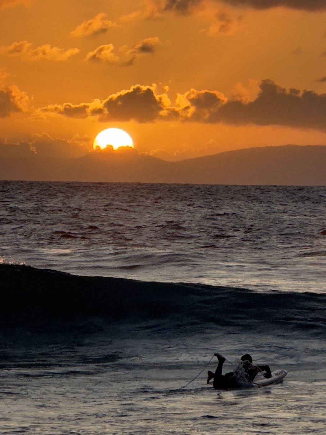 Surfer paddling out at sunset